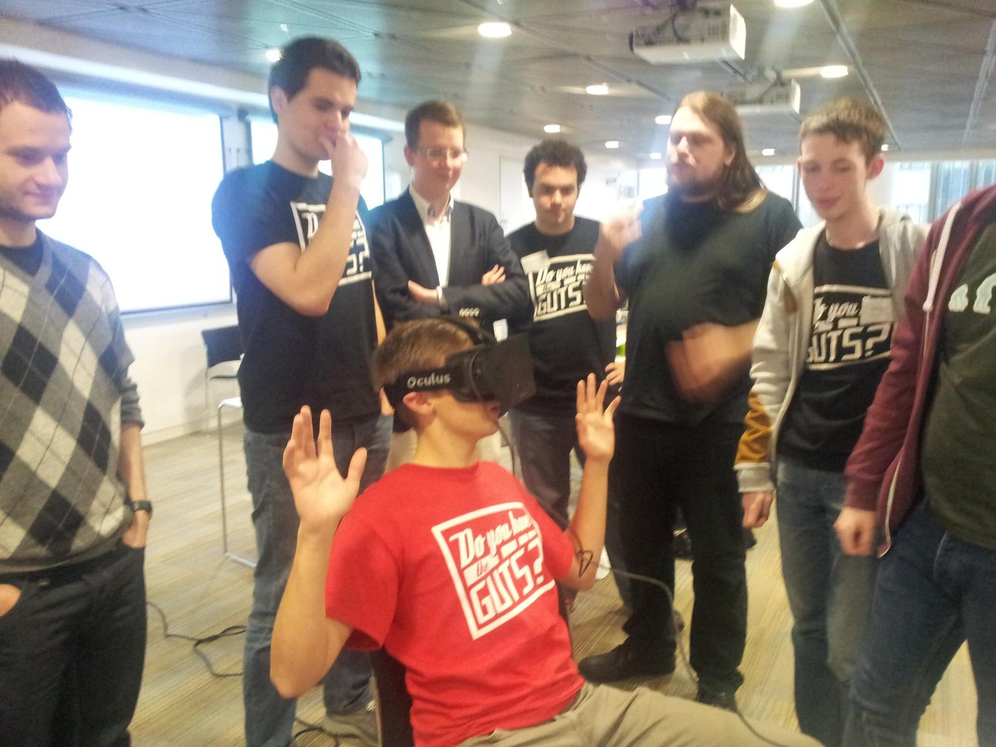 A student in a red GUTS T-shirt wearing an Oculus Rift headset while a group looks on.