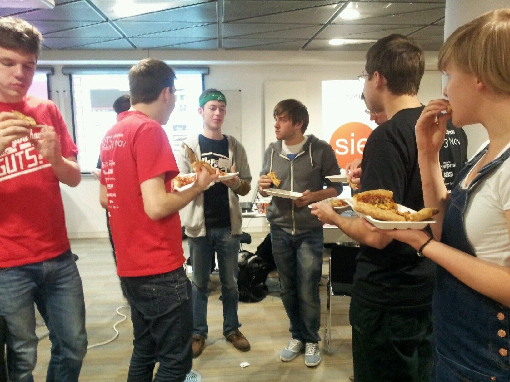 Hackers standing around eating pizza from paper plates.