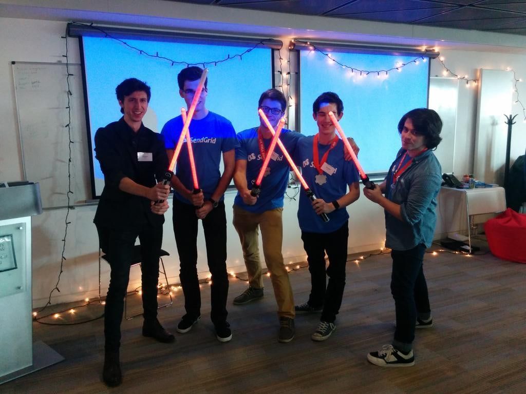 The winning team in front of projector screens and fairy lights, holding glowing toy lightsabers.